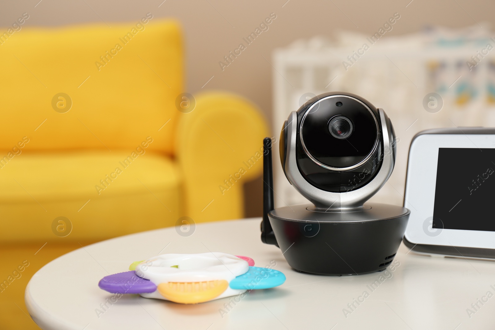 Photo of Modern CCTV security camera, monitor and teether on table in nursery. Space for text