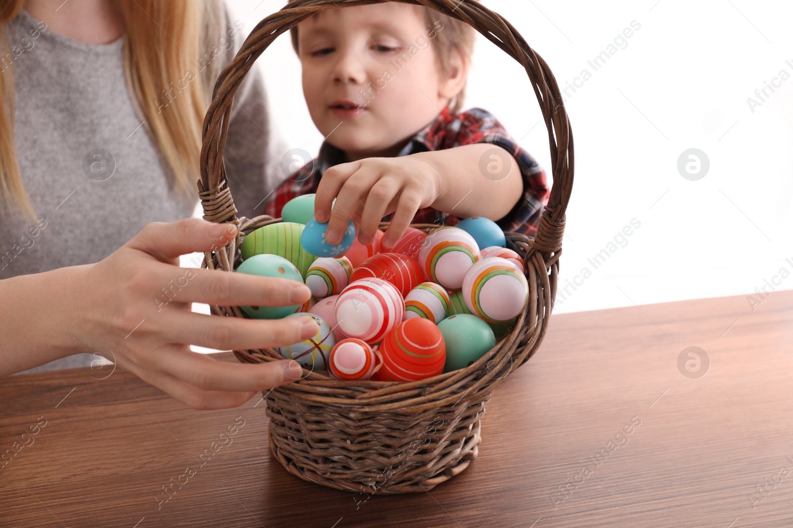 Photo of Little boy and his mother with basket full of dyed Easter eggs at wooden table, closeup. Easter celebration