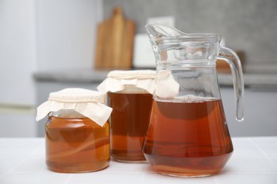 Photo of Homemade fermented kombucha in glass jars and jug on white table in kitchen