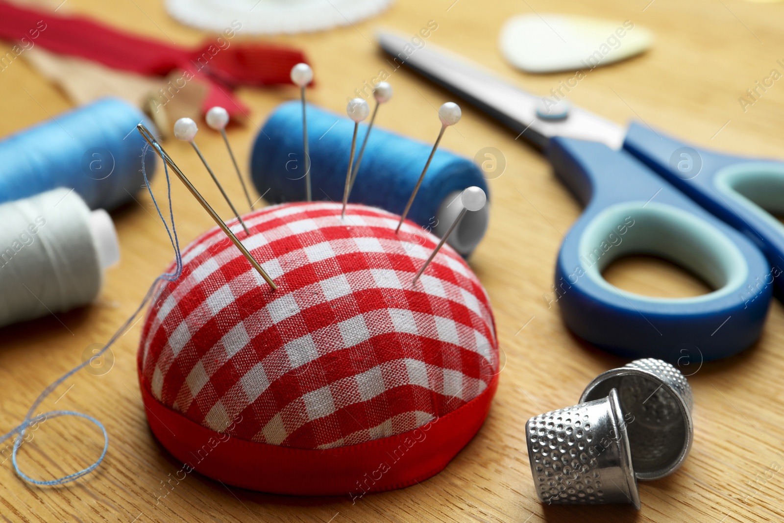 Photo of Pincushion, spools of threads and sewing tools on wooden table, closeup