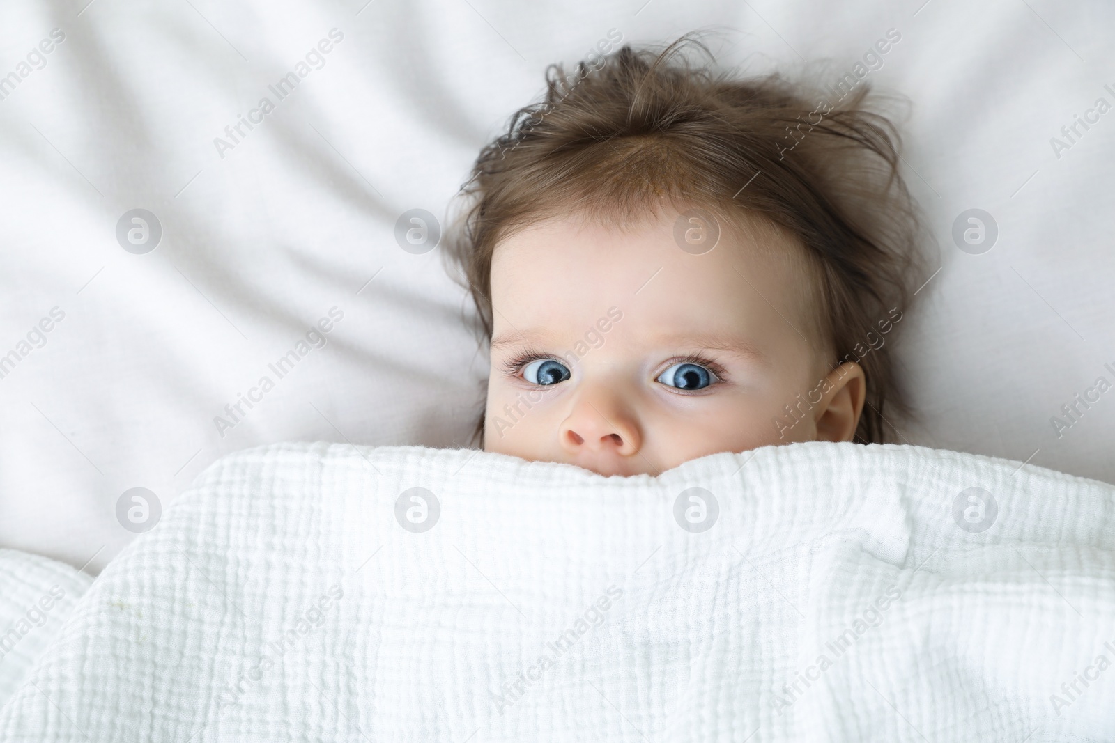 Photo of Cute little baby lying under blanket on soft bed, top view