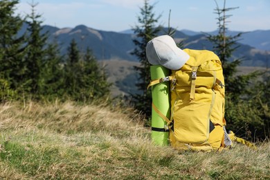 Photo of Backpack with sleeping mat and cap on grassy hill, space for text. Mountain tourism