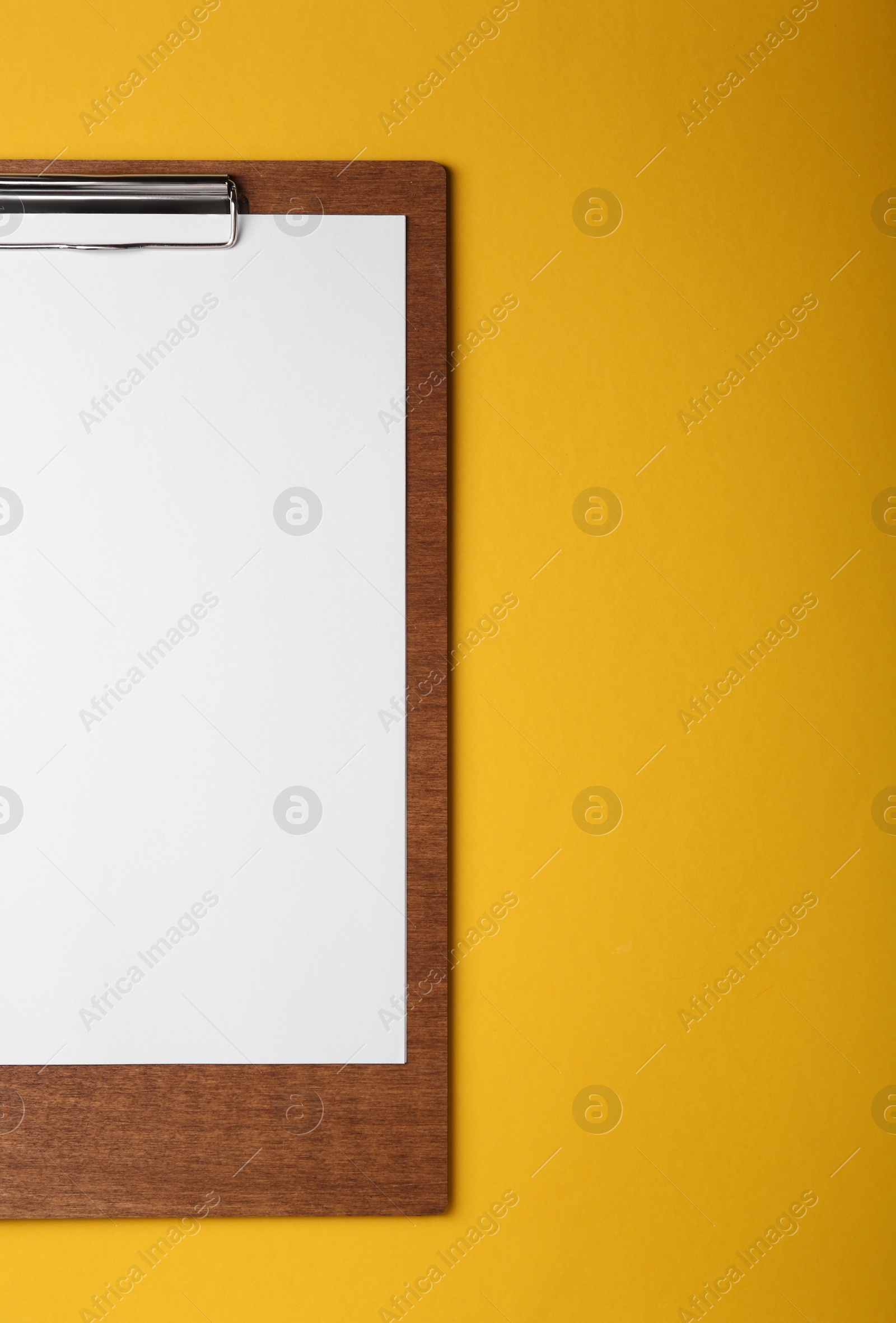 Photo of Wooden clipboard with sheet of blank paper on yellow background, top view. Space for text