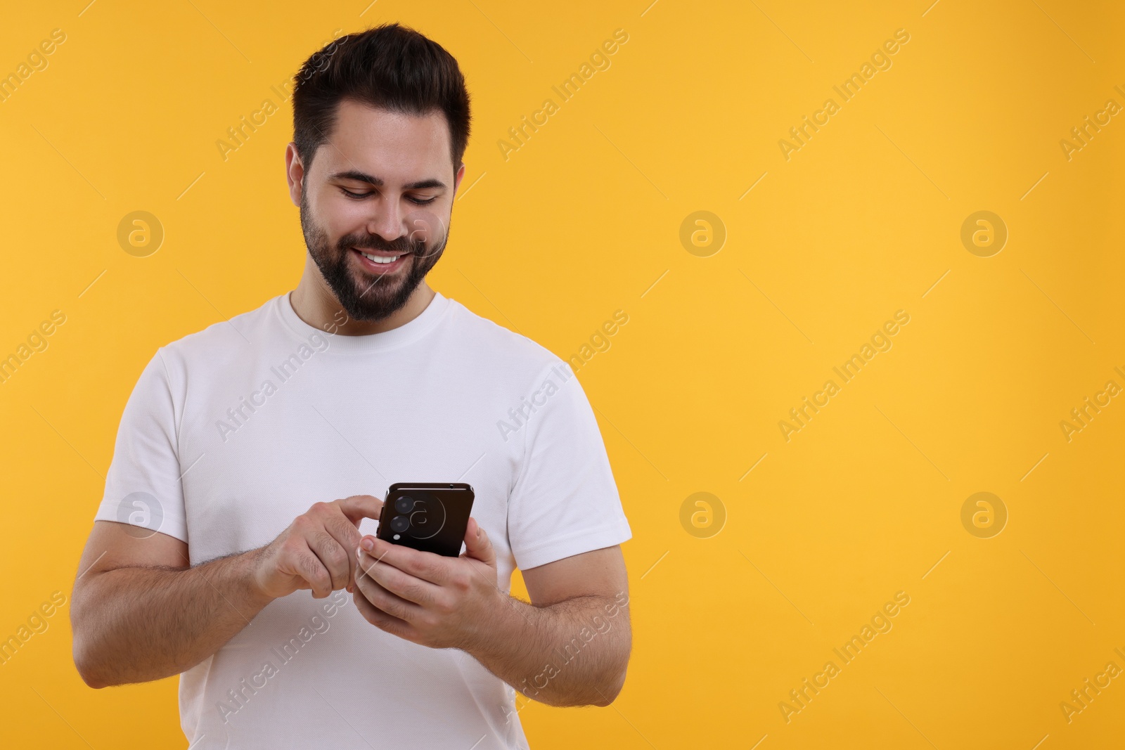 Photo of Happy young man using smartphone on yellow background, space for text