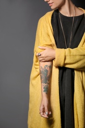 Trendy young woman with tattoo on grey background, closeup