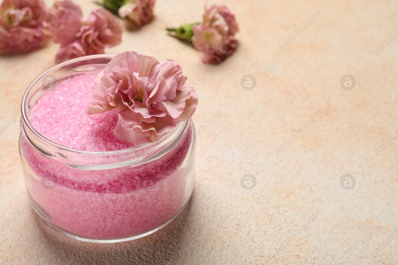 Photo of Aromatic sea salt and flowers on beige textured table, closeup. Space for text