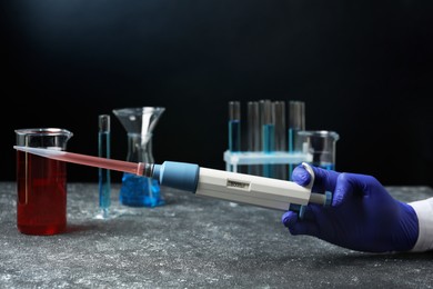 Laboratory analysis. Scientist holding micropipette with liquid at grey table, closeup