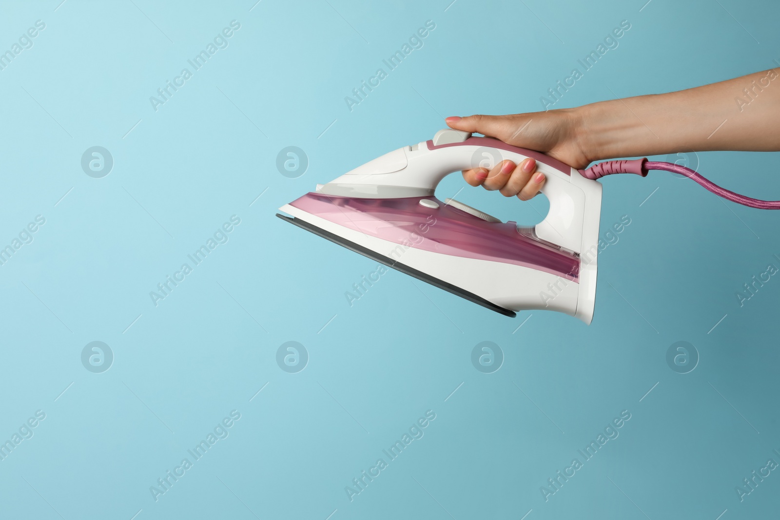 Photo of Woman holding modern iron on turquoise background, closeup. Space for text