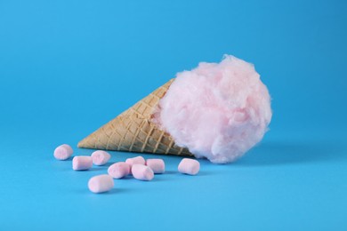 Photo of Sweet cotton candy in waffle cone and marshmallows on light blue background