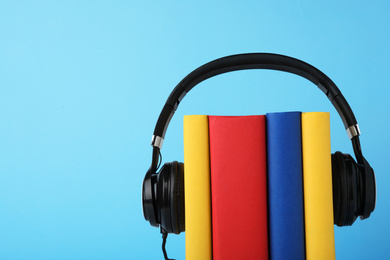 Books and modern headphones on light blue background. Space for text