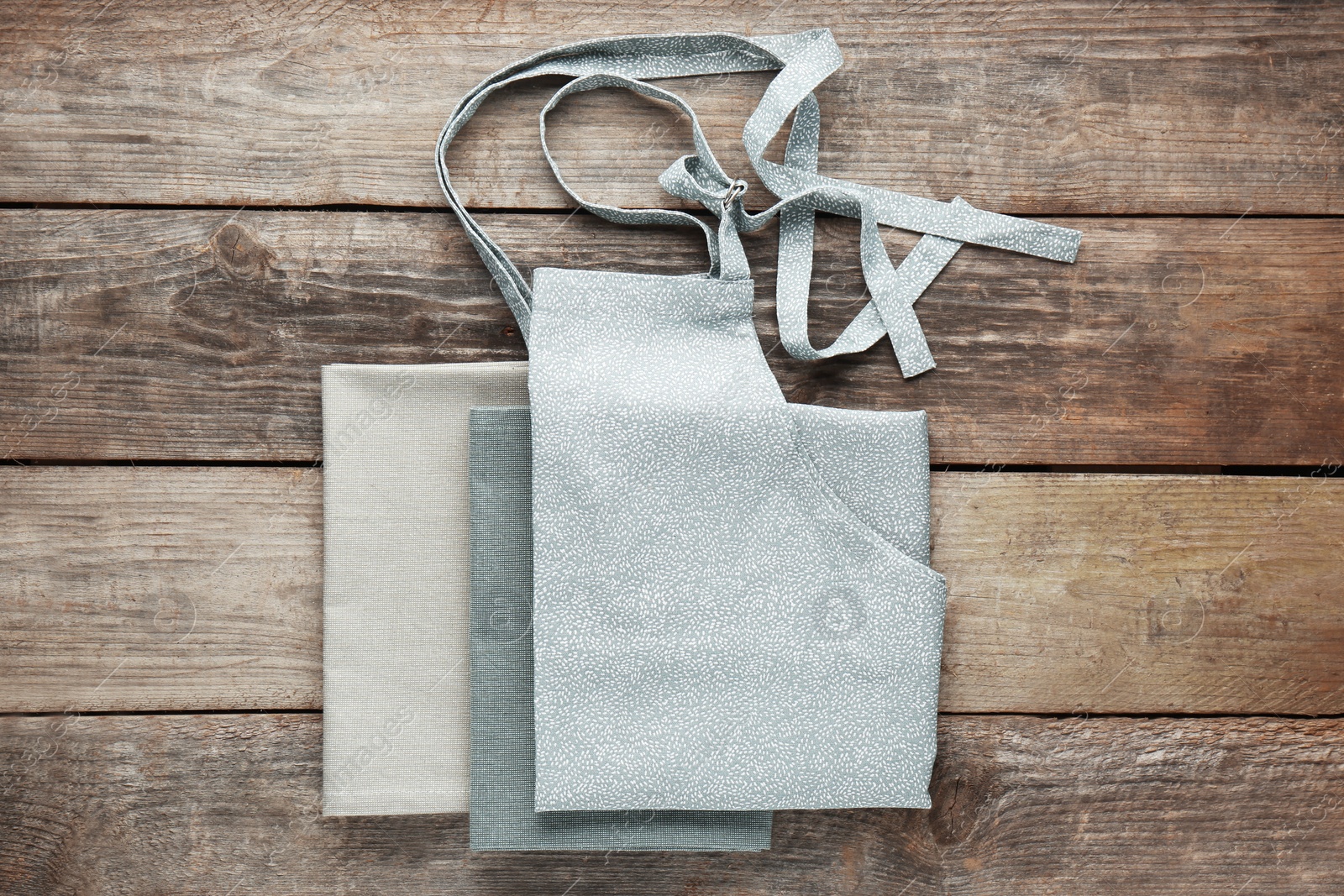 Photo of Grey kitchen napkins and apron on wooden table, flat lay