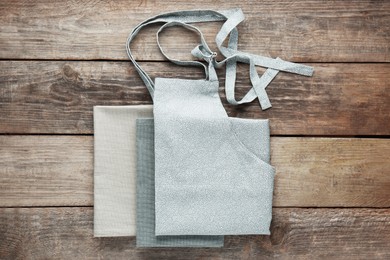 Photo of Grey kitchen napkins and apron on wooden table, flat lay