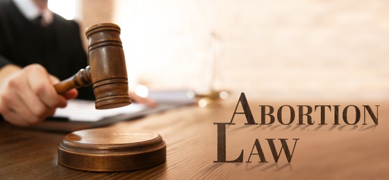 Abortion law. Judge with gavel at wooden table indoors, closeup. Banner design