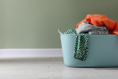 Photo of Laundry basket with clothes near light green wall indoors. Space for text