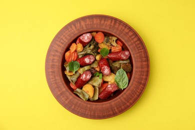 Photo of Delicious sausage and baked vegetables on yellow background, top view