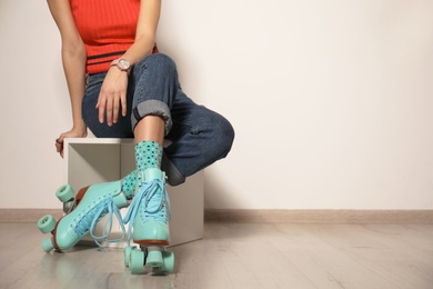 Young woman with retro roller skates against light wall, closeup. Space for text