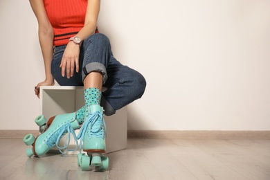 Photo of Young woman with retro roller skates against light wall, closeup. Space for text