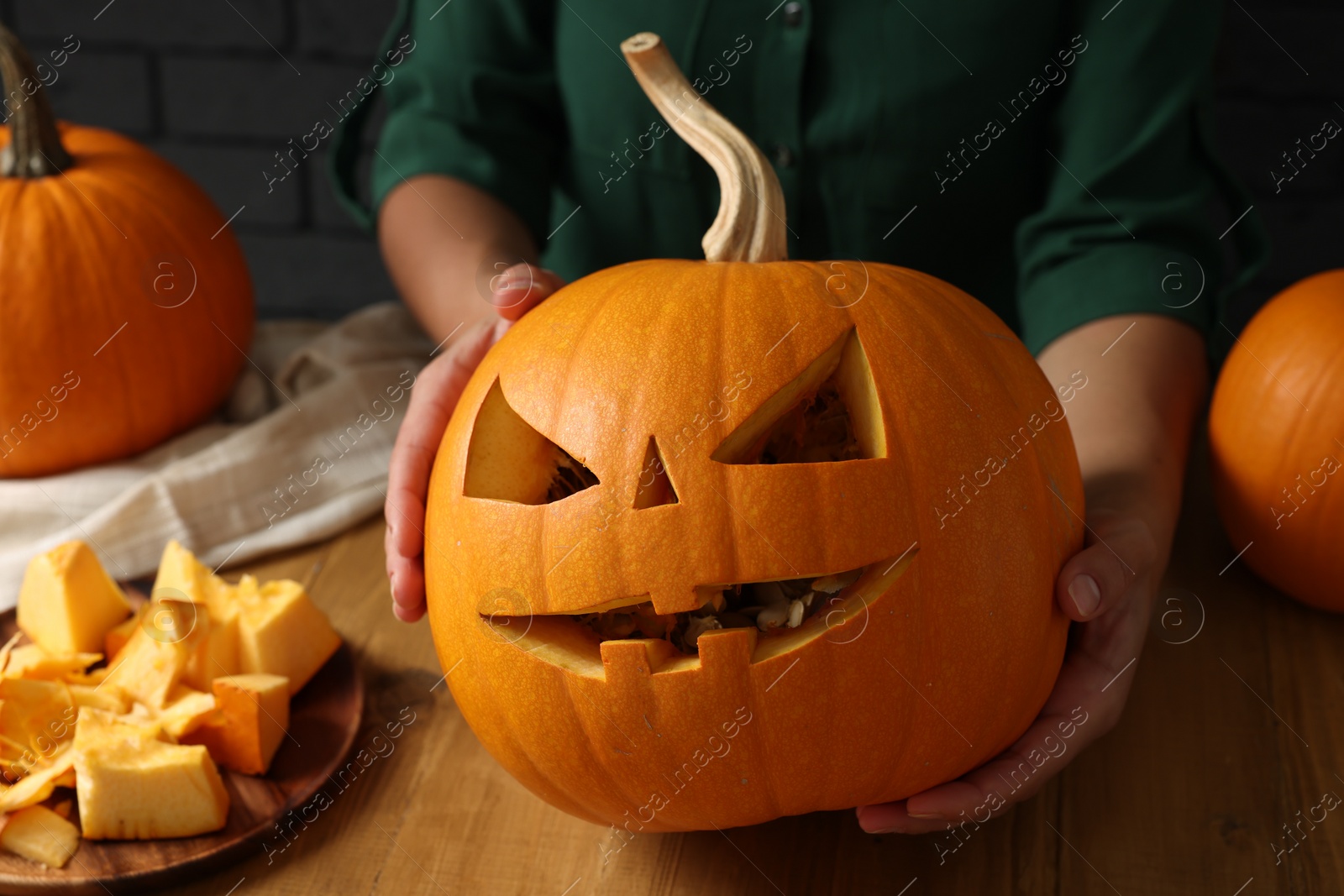 Photo of Woman with carved pumpkin at wooden table, closeup. Halloween celebration