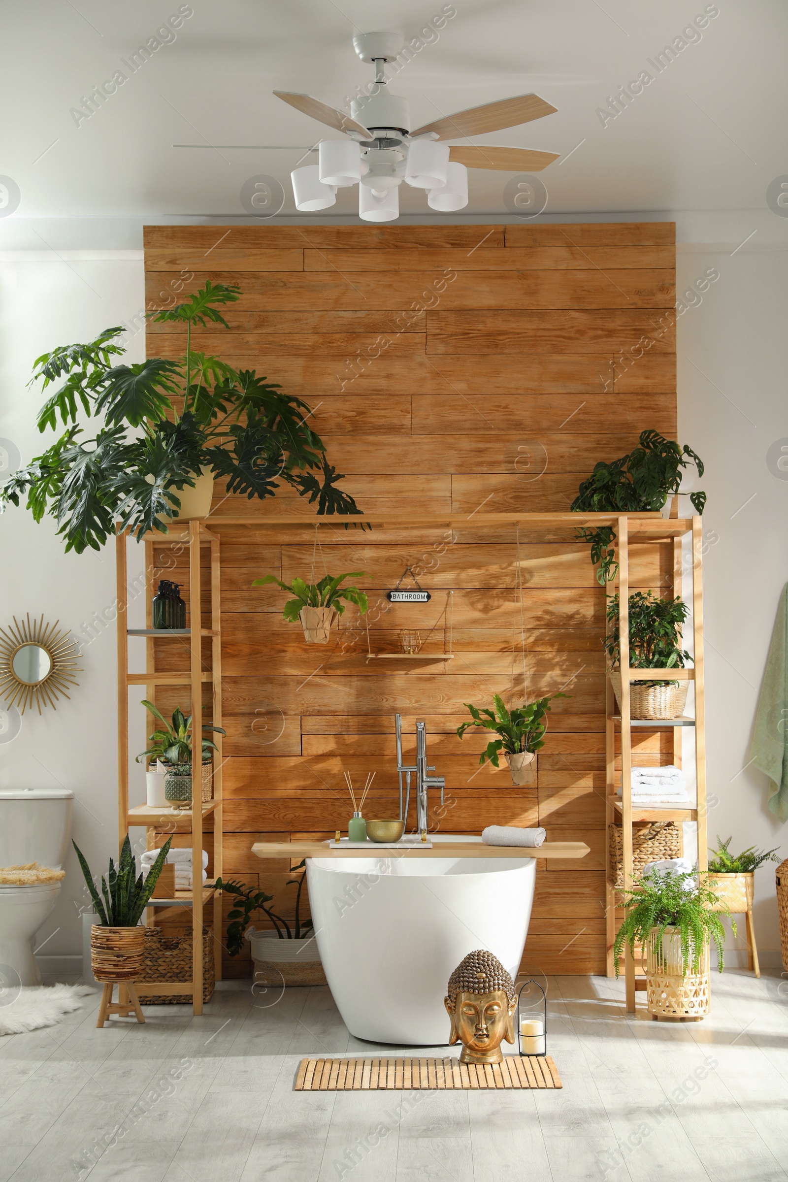 Photo of Stylish bathroom interior with white tub and green houseplants near wooden wall. Idea for design