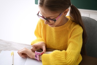 Photo of Girl using stylish smart watch at wooden table in school, closeup