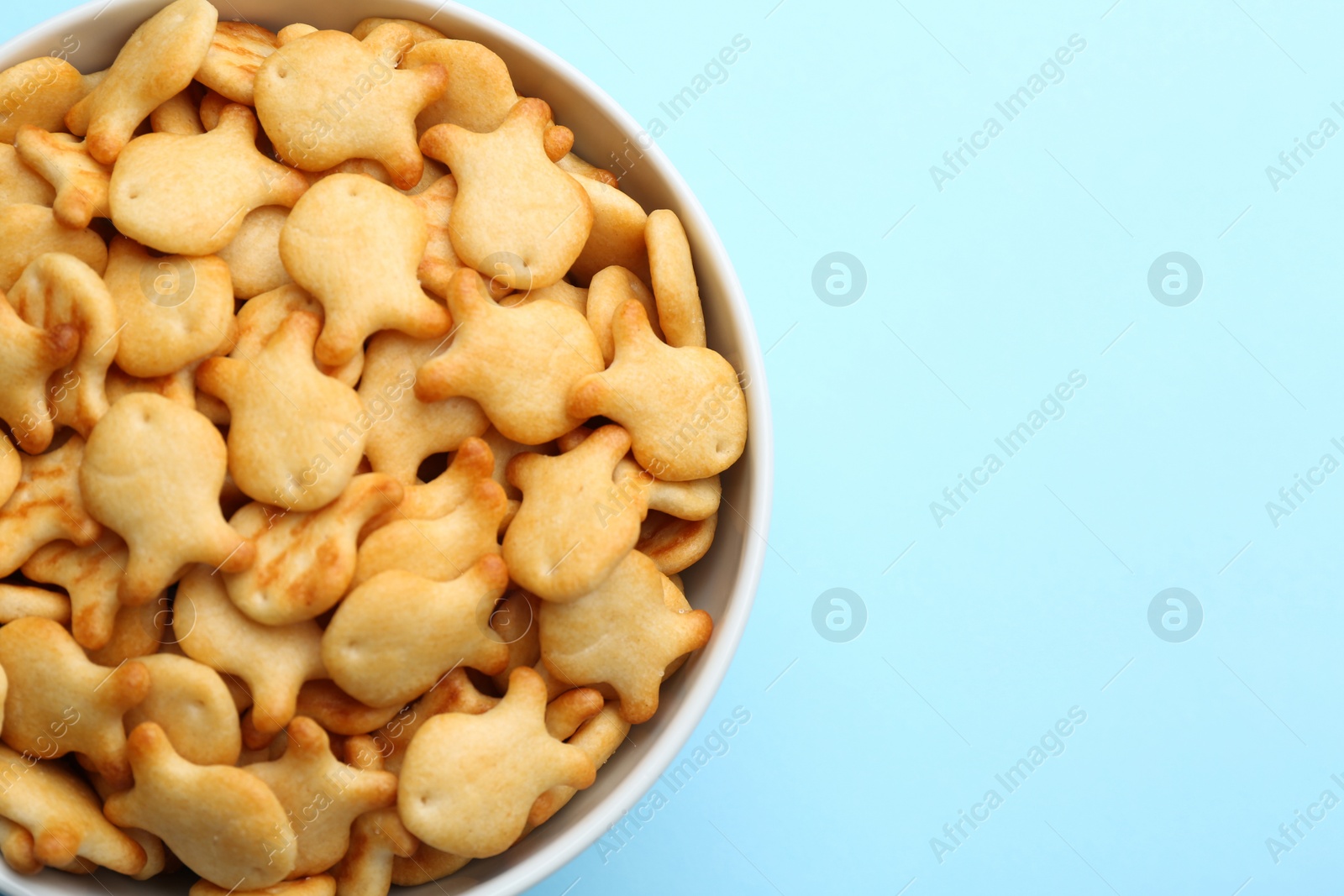 Photo of Delicious goldfish crackers in bowl on light blue background, top view. Space for text