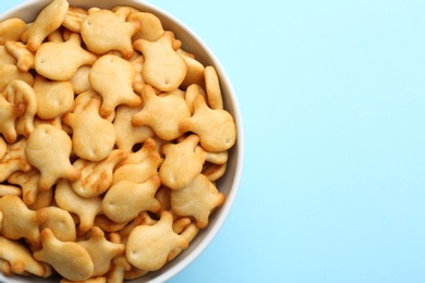 Photo of Delicious goldfish crackers in bowl on light blue background, top view. Space for text