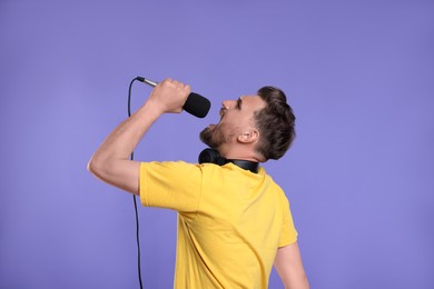 Photo of Handsome man with microphone singing on violet background