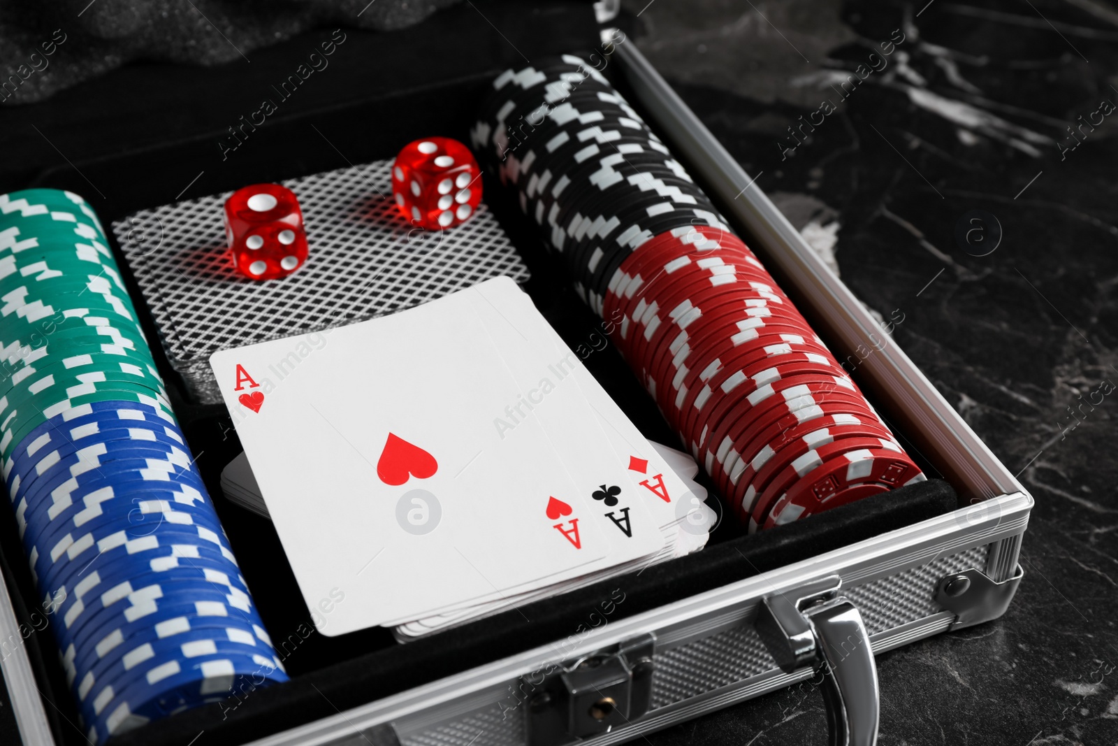 Photo of Gaming chips, dices and cards in suitcase on dark marble table