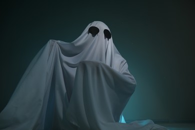 Photo of Creepy ghost. Woman covered with sheet on dark teal background, low angle view. Space for text