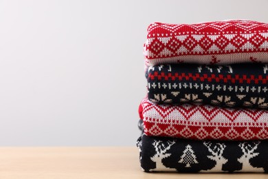 Stack of different Christmas sweaters on table against light background. Space for text