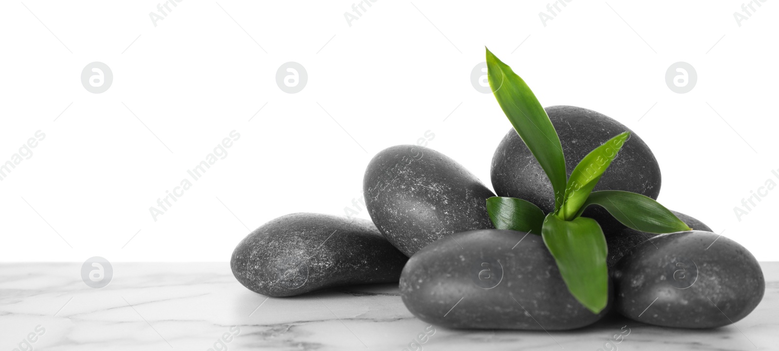 Photo of Black spa stones with bamboo on table against white background. Space for text