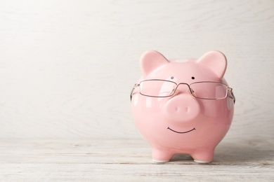 Photo of Piggy bank with glasses on light table. Space for text
