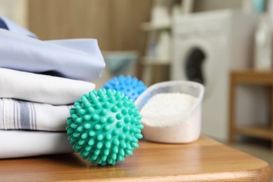 Photo of Dryer balls near stacked clean clothes and detergent on wooden table in laundry room, closeup. Space for text