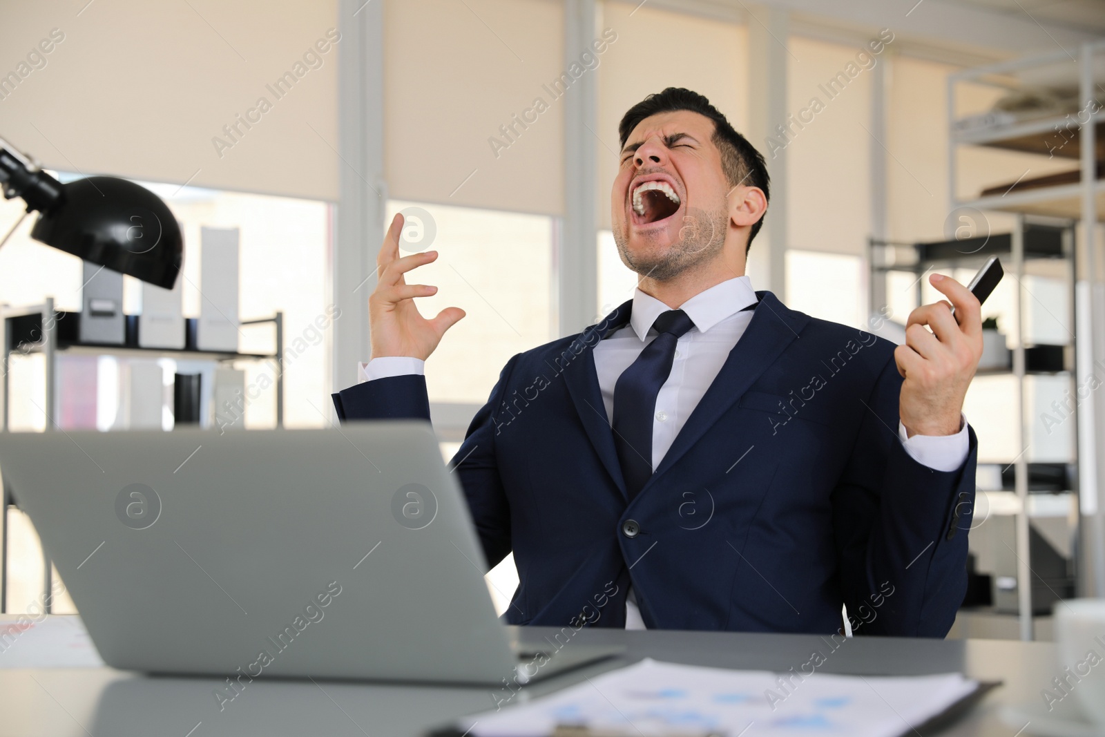 Photo of Emotional businessman with laptop and smartphone at table in office