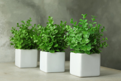 Photo of Artificial plants in white flower pots on light stone table