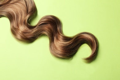 Photo of Lock of brown wavy hair on color background, top view