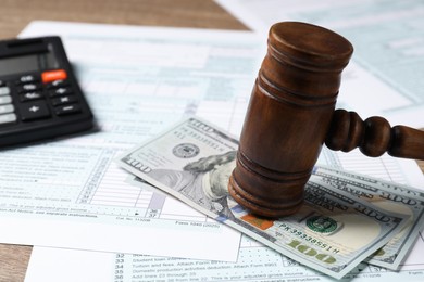 Tax return forms, dollar banknotes, gavel and calculator on wooden table, closeup