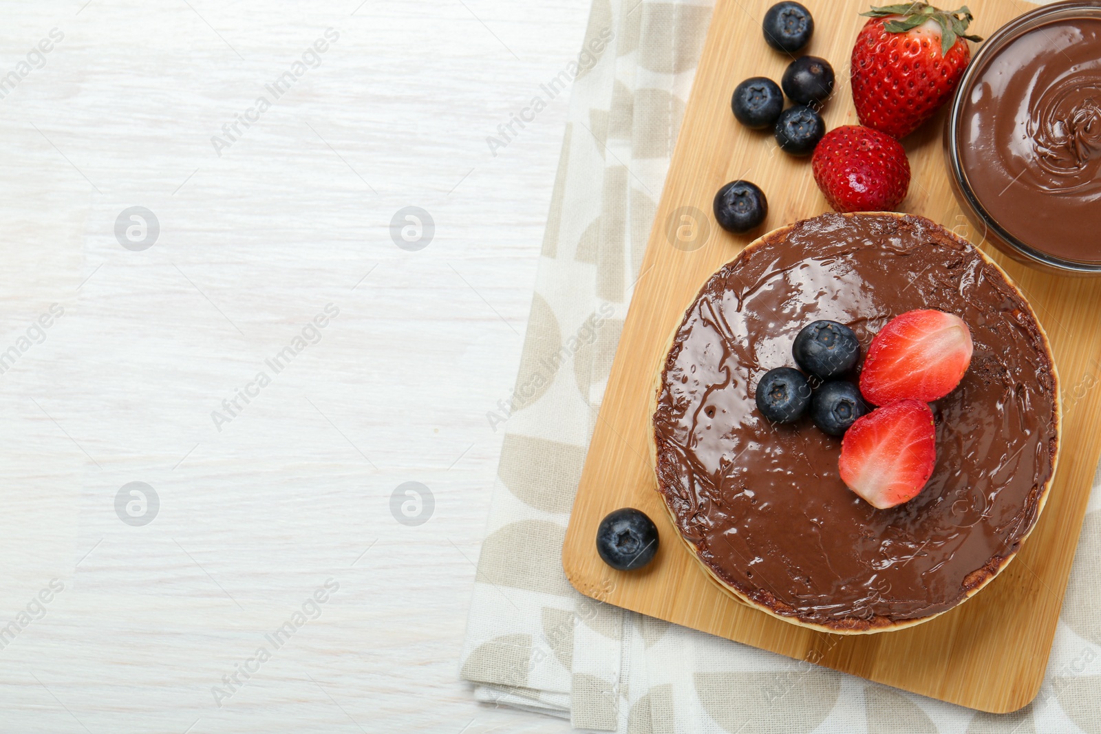 Photo of Tasty pancakes with chocolate paste and berries on white wooden table, top view. Space for text