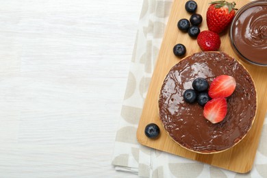 Tasty pancakes with chocolate paste and berries on white wooden table, top view. Space for text