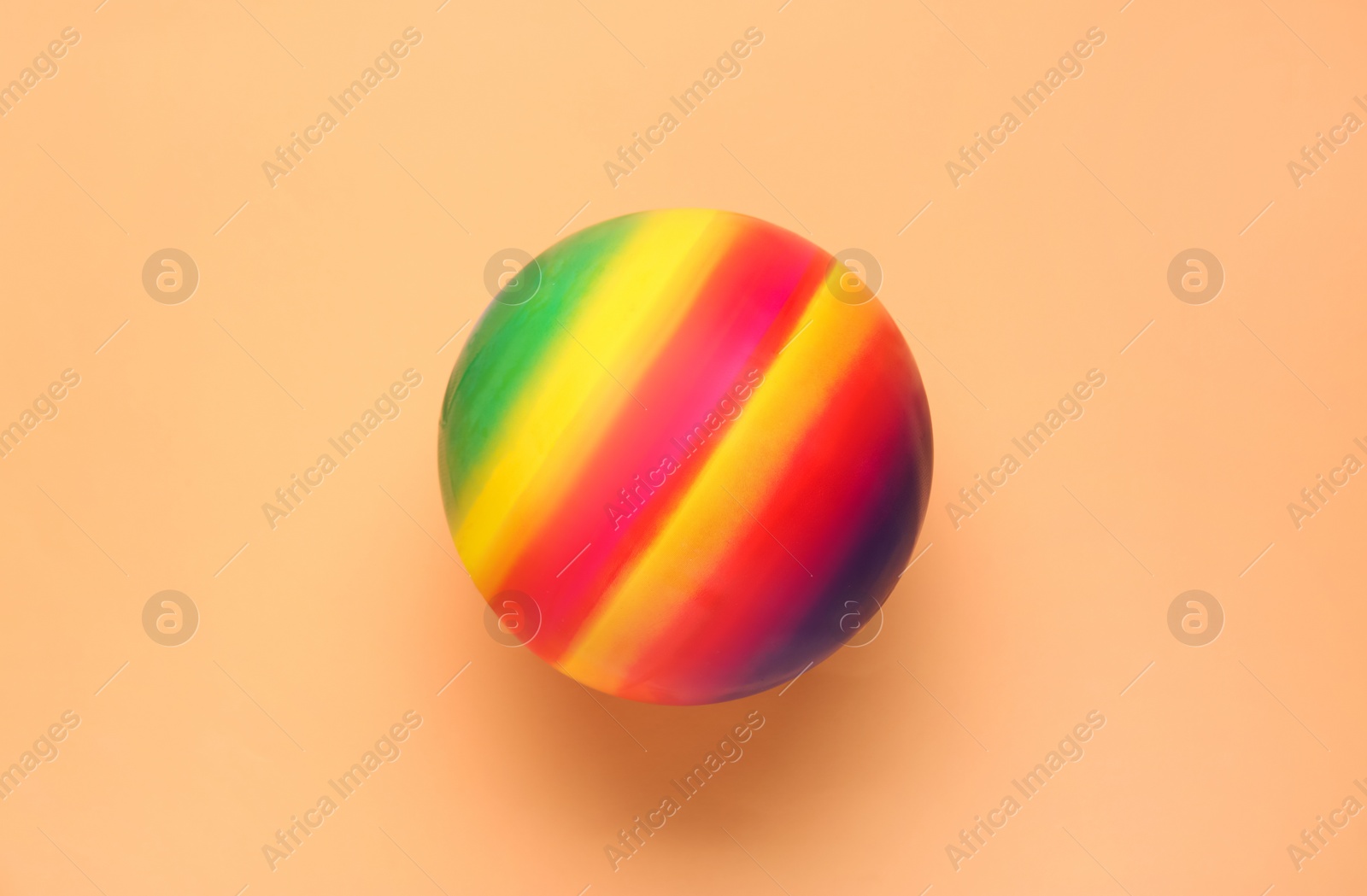 Photo of Bright rubber kids' ball on pale orange background, top view