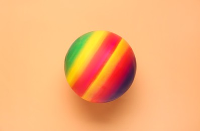 Bright rubber kids' ball on pale orange background, top view