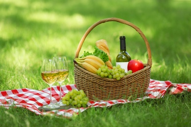 Photo of Wicker basket with food and wine on blanket in park. Summer picnic
