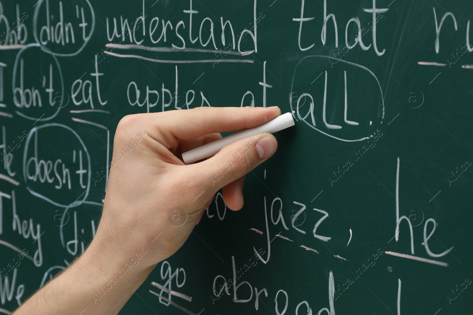 Photo of English teacher writing with chalk on green chalkboard, closeup