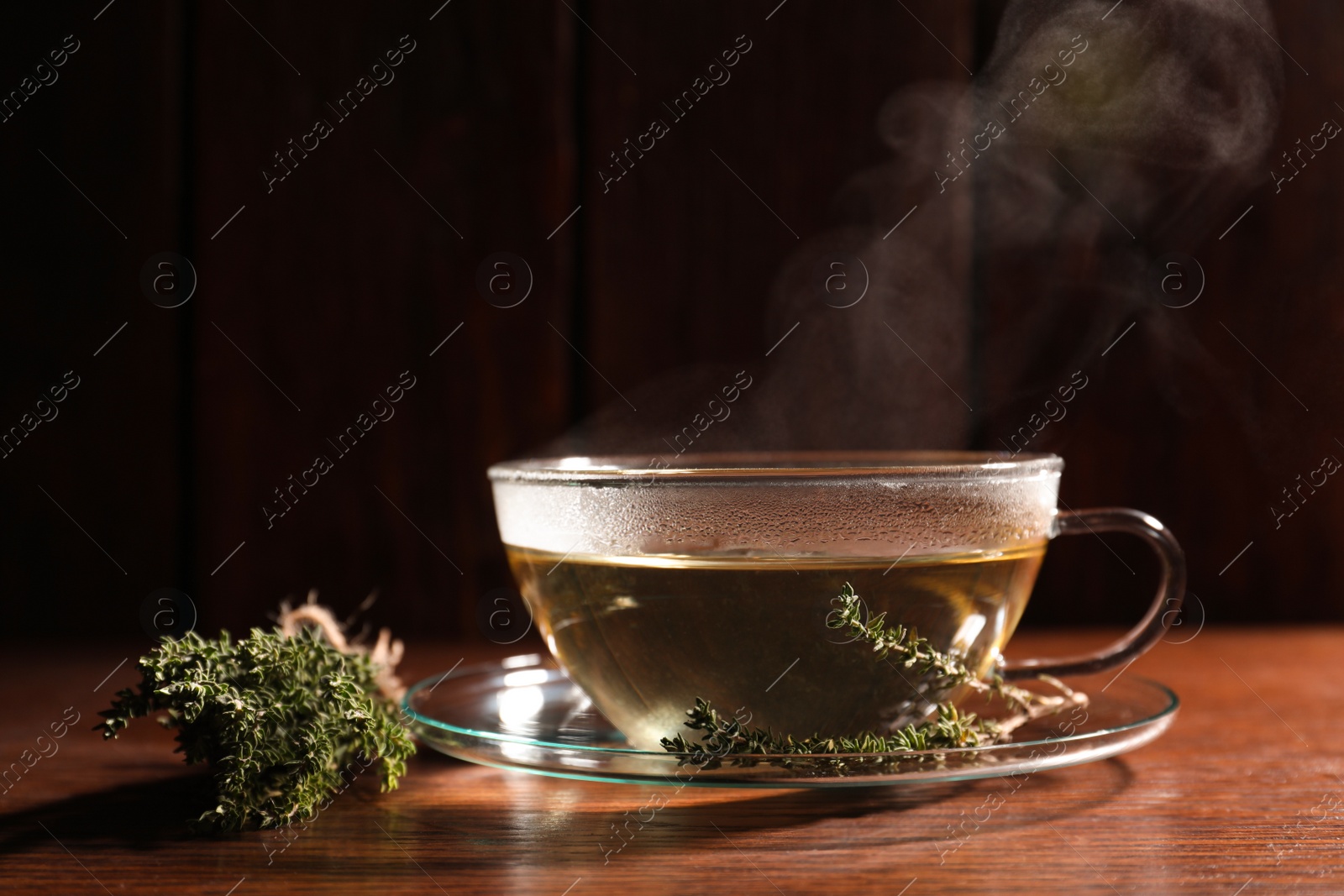 Photo of Cup of aromatic herbal tea and thyme on wooden table