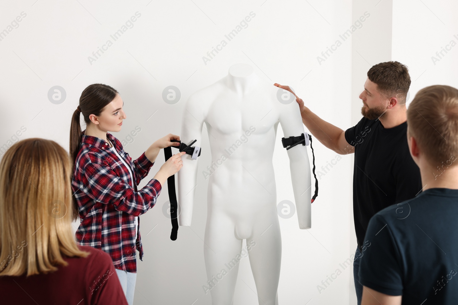 Photo of Group of people learning how to apply medical tourniquet on mannequin indoors