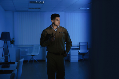 Photo of Professional security guard with portable radio set in dark office