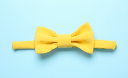 Photo of Stylish yellow bow tie on light blue background, top view