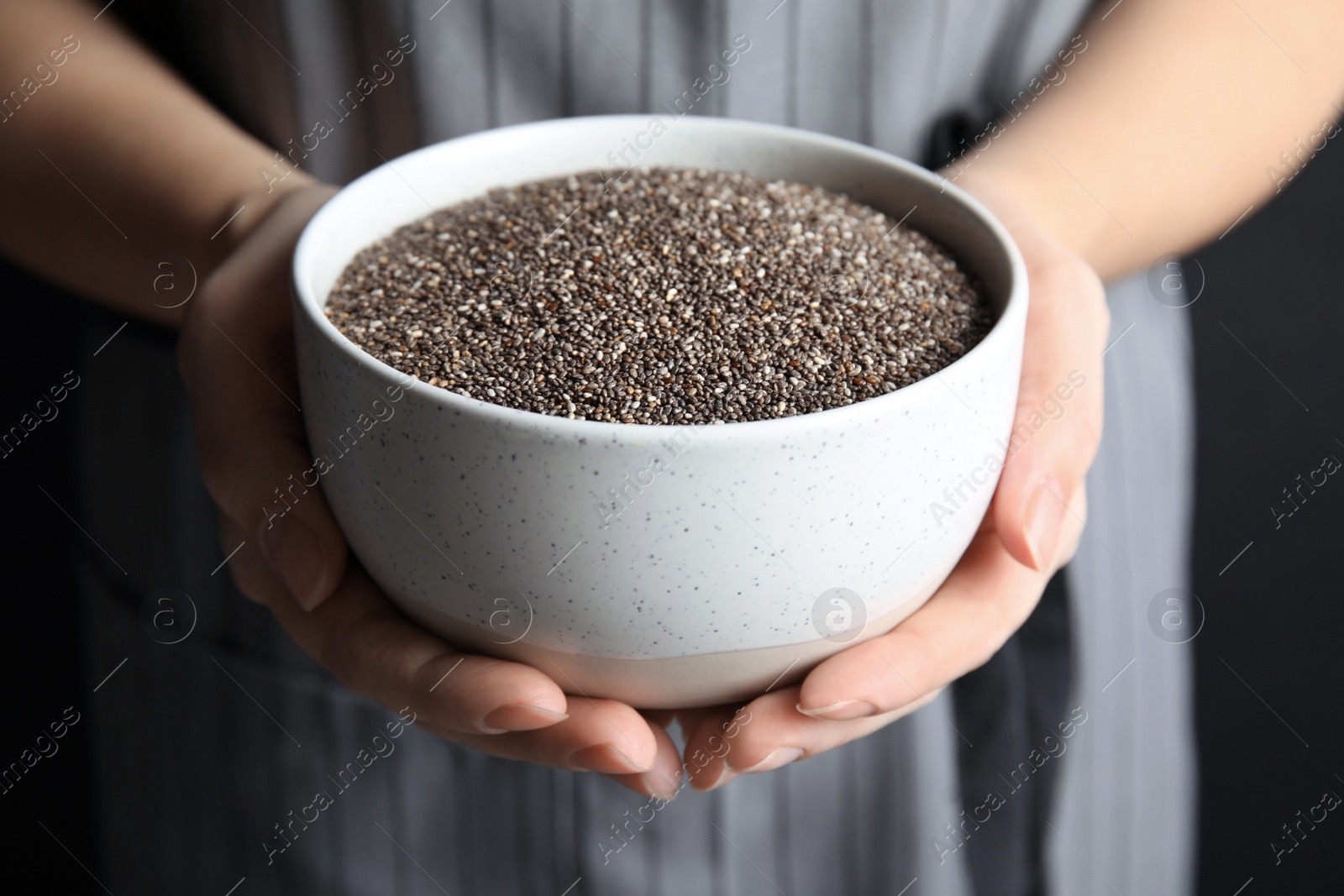 Photo of Woman holding bowl with chia seeds on dark background, closeup