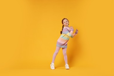 Cute little girl dancing on orange background