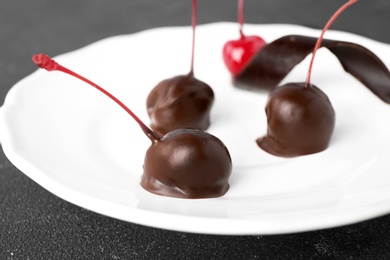 Photo of Plate of chocolate dipped cherries on black table, closeup